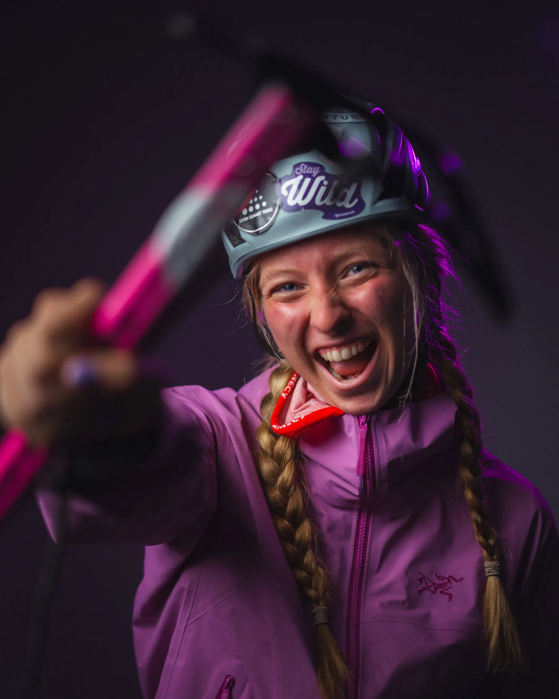 Bianca laughing in a purple jacket, holding out a pink ice axe